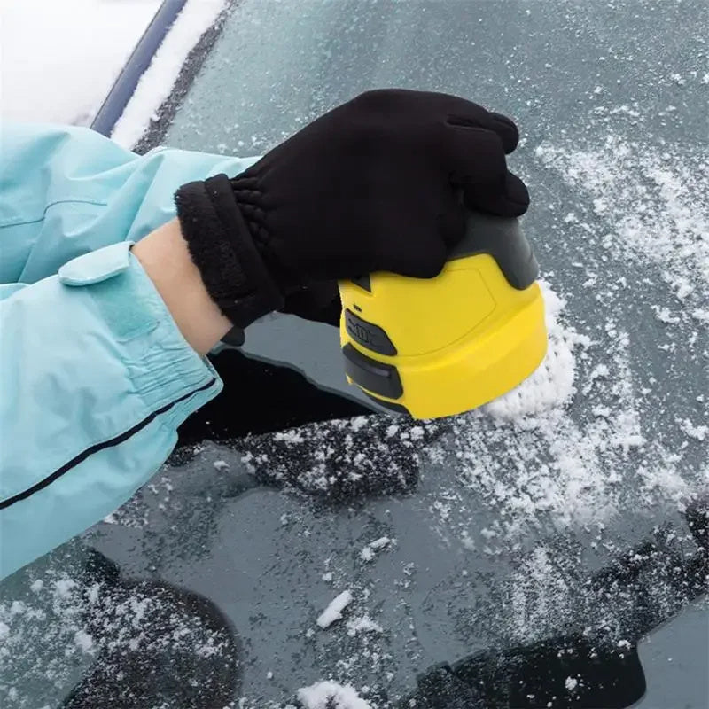 Hand using a cordless electric snow scraper to remove ice from a car windshield in winter conditions.