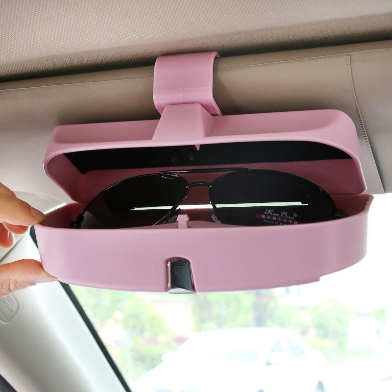 Pink sunglasses holder attached to a car's sun visor with sunglasses inside.